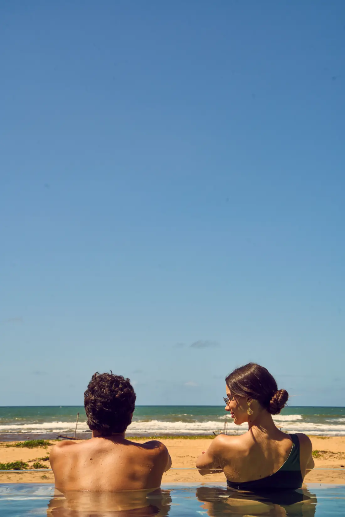Casal na piscina de borda infinita observando o mar